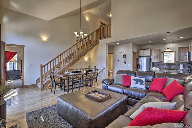 living room with baseboards, light wood finished floors, a high ceiling, stairs, and a chandelier