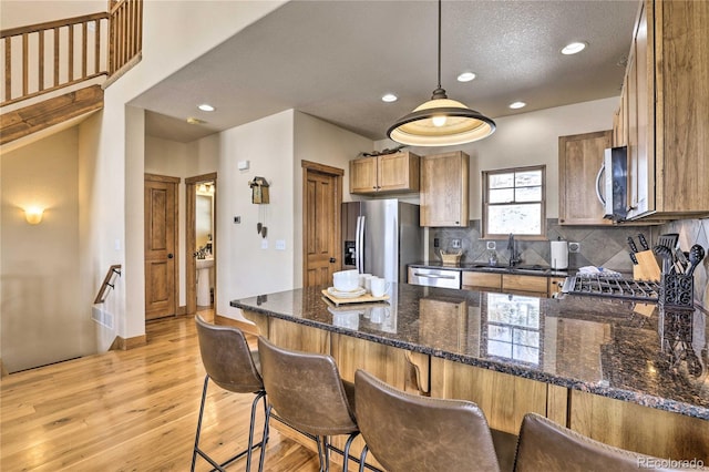 kitchen with a peninsula, light wood-style flooring, a sink, appliances with stainless steel finishes, and backsplash