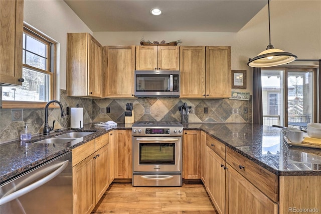 kitchen with a peninsula, light wood-style flooring, a sink, decorative backsplash, and stainless steel appliances