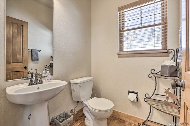 half bathroom featuring toilet, wood finished floors, baseboards, and a textured wall