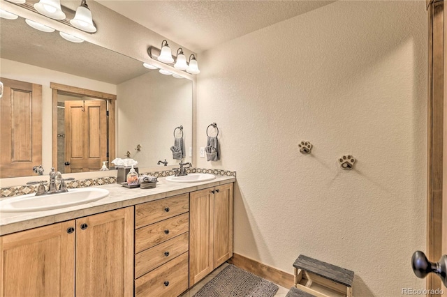 full bath featuring double vanity, a textured wall, baseboards, and a sink