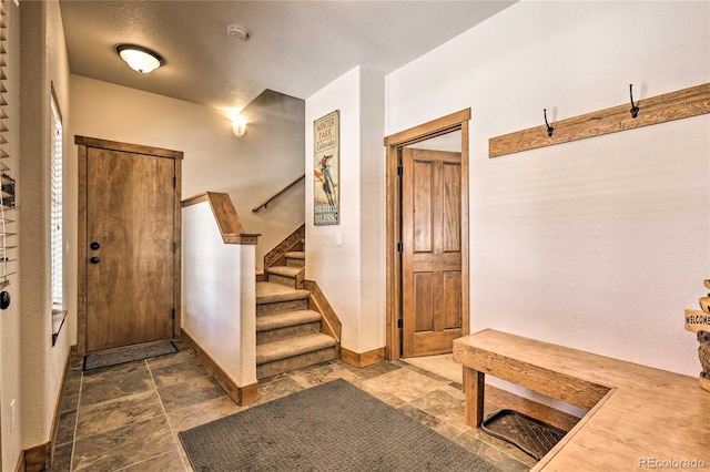 foyer with stairs, baseboards, and stone finish flooring