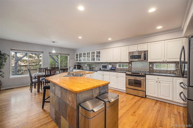 kitchen with pendant lighting, sink, appliances with stainless steel finishes, white cabinets, and a center island with sink