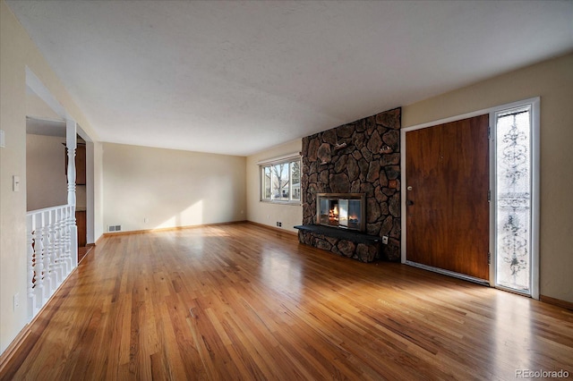 unfurnished living room featuring a stone fireplace, a wealth of natural light, and light hardwood / wood-style flooring