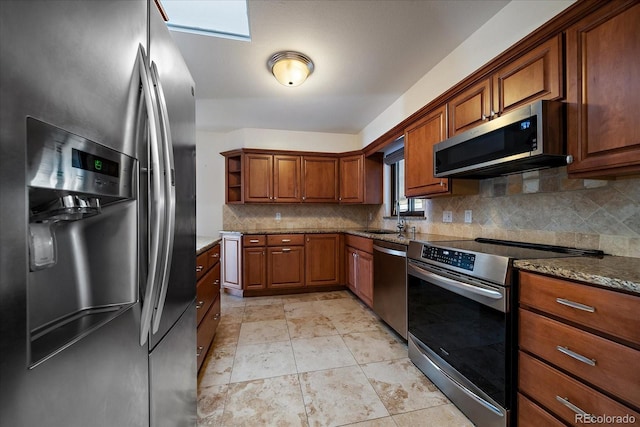 kitchen with appliances with stainless steel finishes, a skylight, tasteful backsplash, dark stone counters, and sink