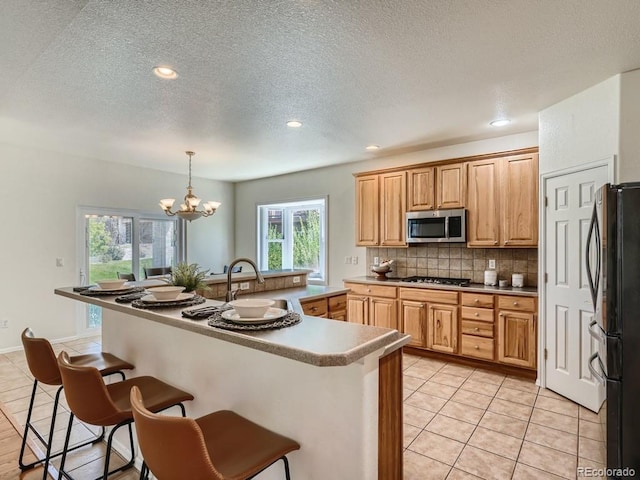 7746 S Valdai Ct, Aurora, CO 80016 - kitchen featuring stainless steel microwave, freestanding refrigerator, a breakfast bar, tasteful backsplash, and a textured ceiling