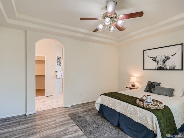 7746 S Valdai Ct, Aurora, CO 80016 - bedroom featuring a tray ceiling, arched walkways, wood finished floors, ceiling fan, and a walk in closet