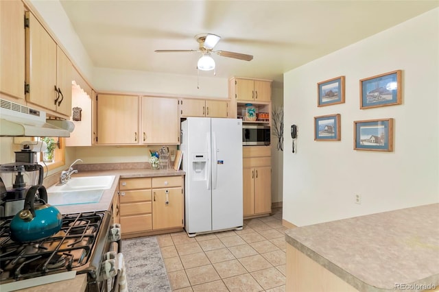 kitchen featuring appliances with stainless steel finishes, light countertops, light brown cabinetry, under cabinet range hood, and a sink