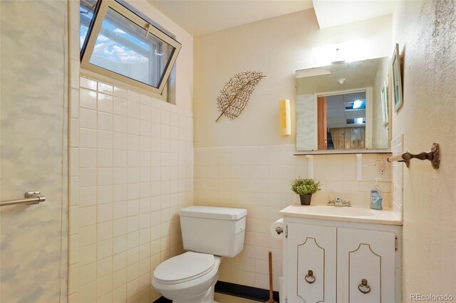 bathroom with toilet, a wainscoted wall, vanity, and tile walls