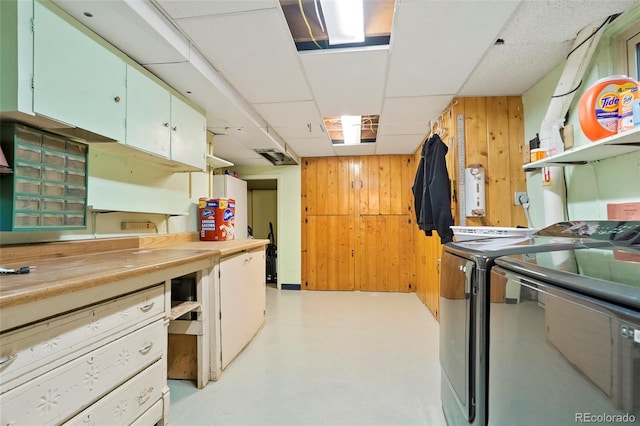 kitchen featuring finished concrete flooring, independent washer and dryer, light countertops, a paneled ceiling, and wood walls