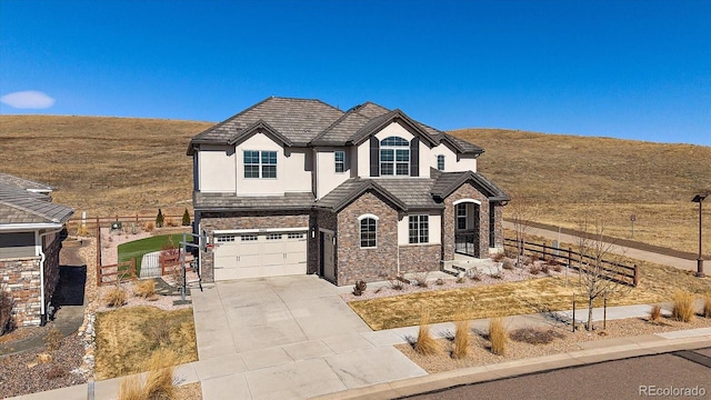 view of front of home featuring stucco siding, fence, a garage, stone siding, and driveway