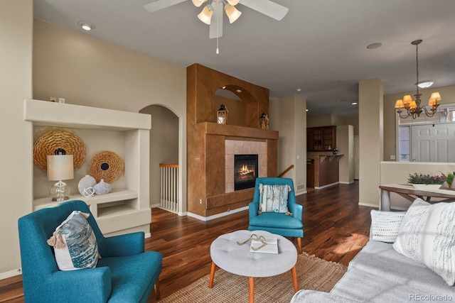 living room with dark hardwood / wood-style flooring, ceiling fan with notable chandelier, and a tile fireplace