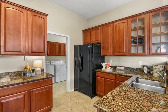 kitchen with sink, black fridge, dark stone countertops, light tile patterned floors, and washer and clothes dryer