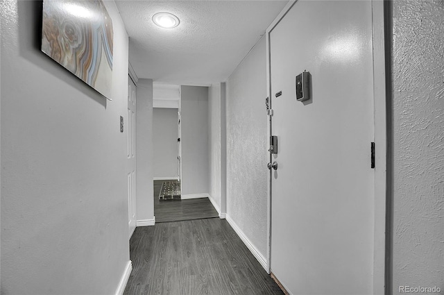 corridor with a textured ceiling, a textured wall, dark wood-style flooring, and baseboards