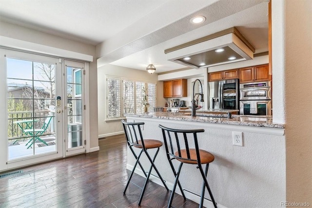 9109 Ironwood Way, Highlands Ranch, CO 80129 - kitchen with plenty of natural light, brown cabinetry, a breakfast bar, visible vents, and appliances with stainless steel finishes