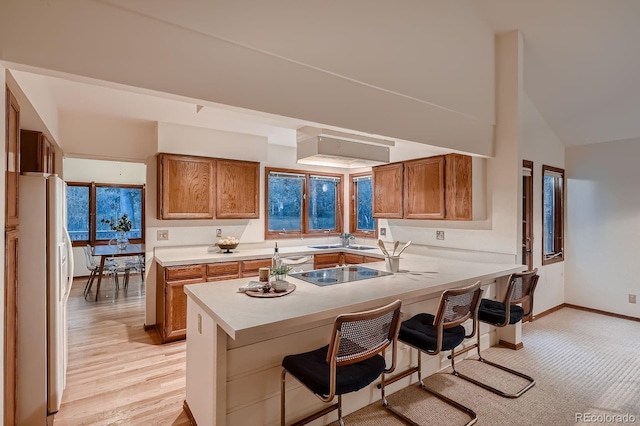 kitchen with brown cabinetry, a sink, a peninsula, black electric stovetop, and white fridge with ice dispenser