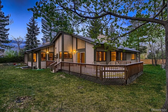 rear view of property featuring a deck, stucco siding, a chimney, a sunroom, and a lawn