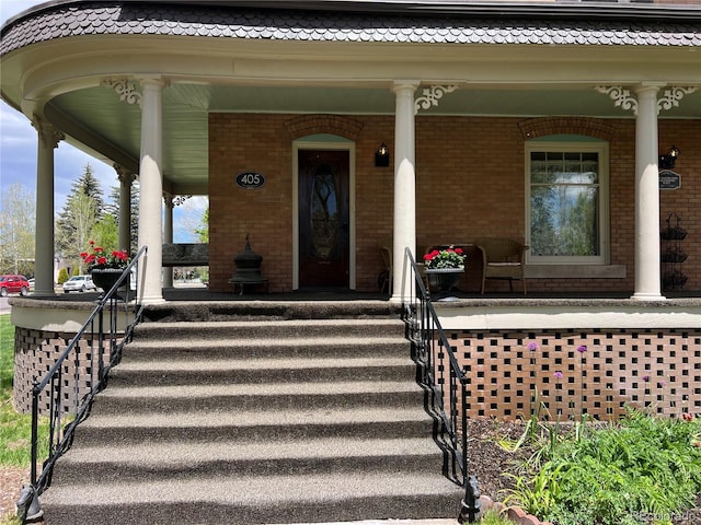 view of exterior entry featuring covered porch and brick siding