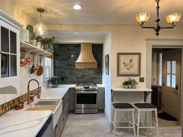 kitchen featuring gas stove, custom range hood, a sink, decorative backsplash, and light stone counters