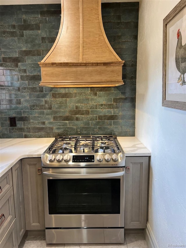 kitchen featuring stainless steel range with gas stovetop, gray cabinetry, custom range hood, and light countertops