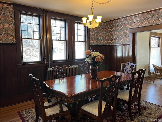 dining area with a chandelier, radiator heating unit, wood finished floors, a wainscoted wall, and wallpapered walls