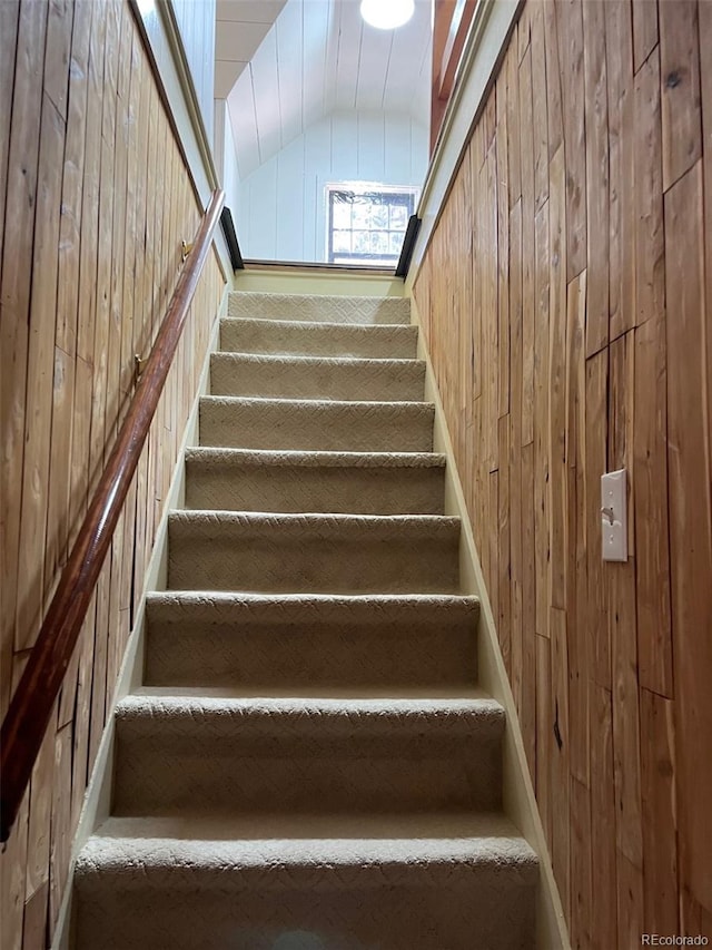 stairway featuring lofted ceiling and wood walls