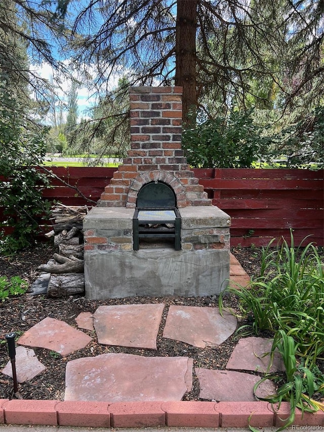 view of patio with an outdoor brick fireplace and fence
