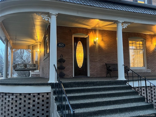 doorway to property with covered porch and brick siding