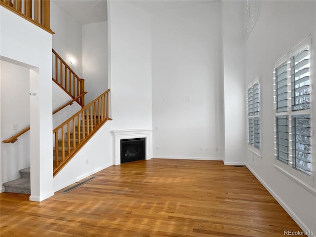 unfurnished living room featuring wood-type flooring and a towering ceiling