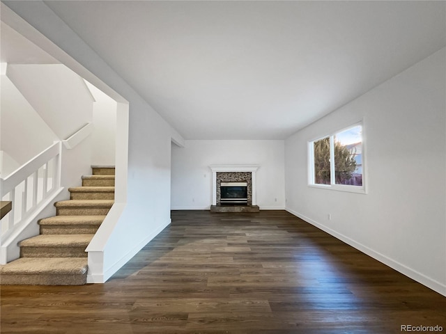 unfurnished living room featuring dark wood-type flooring and a stone fireplace