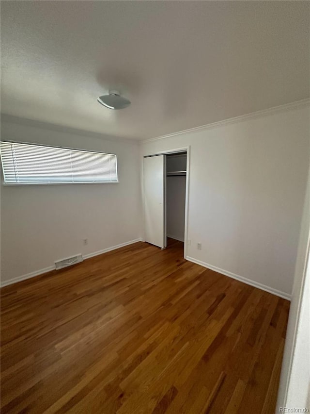 unfurnished bedroom featuring a closet, dark hardwood / wood-style flooring, and crown molding