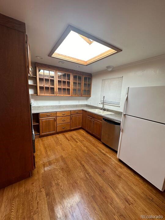 kitchen featuring a skylight, sink, stainless steel dishwasher, white fridge, and light wood-type flooring