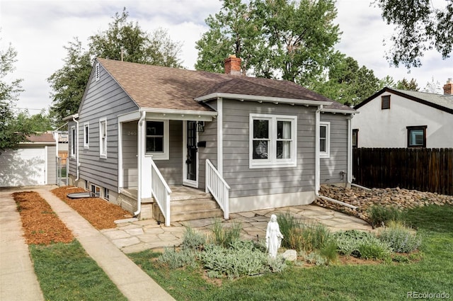 bungalow-style house with fence, a chimney, a shingled roof, and driveway
