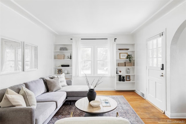 living room with arched walkways, light wood finished floors, and built in features
