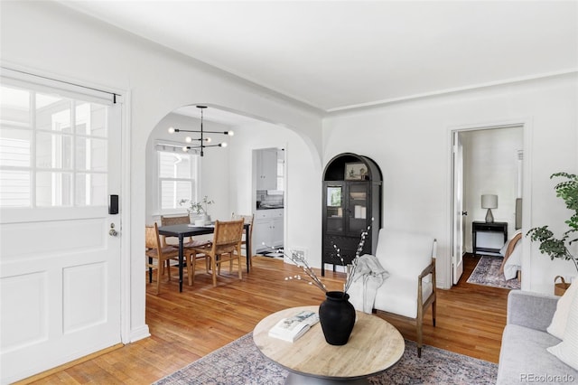 living area with arched walkways, light wood-style flooring, and a chandelier