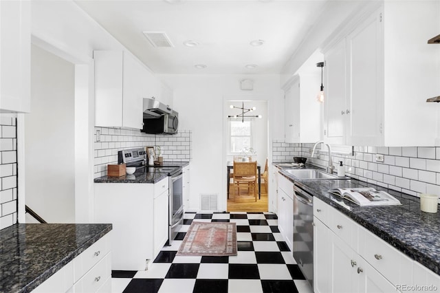 kitchen featuring a sink, appliances with stainless steel finishes, dark flooring, white cabinetry, and backsplash