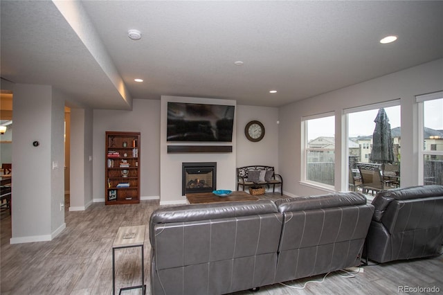 living area with a fireplace, recessed lighting, light wood-style flooring, a textured ceiling, and baseboards