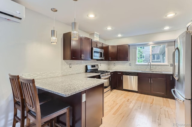 kitchen featuring a wall mounted AC, stainless steel appliances, a kitchen breakfast bar, kitchen peninsula, and light hardwood / wood-style floors