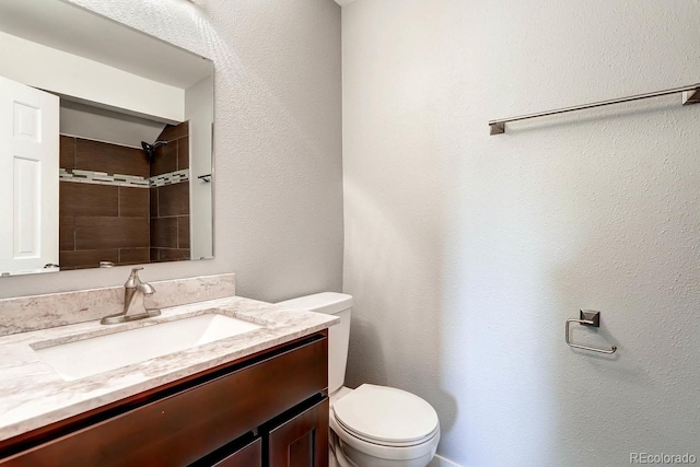 bathroom with toilet, a tile shower, and vanity