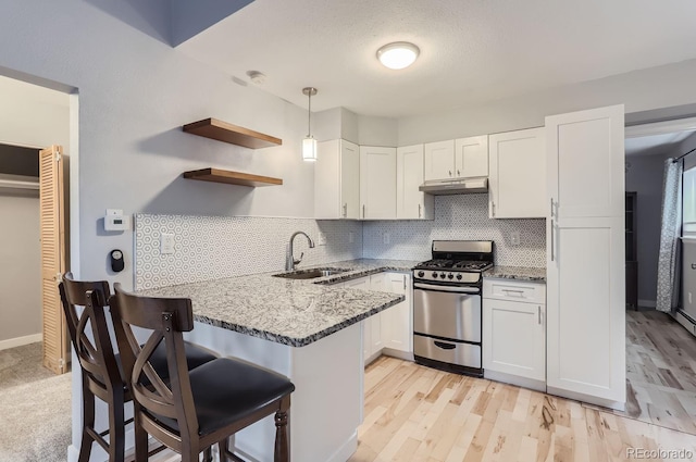 kitchen featuring gas stove, decorative light fixtures, sink, kitchen peninsula, and a breakfast bar area