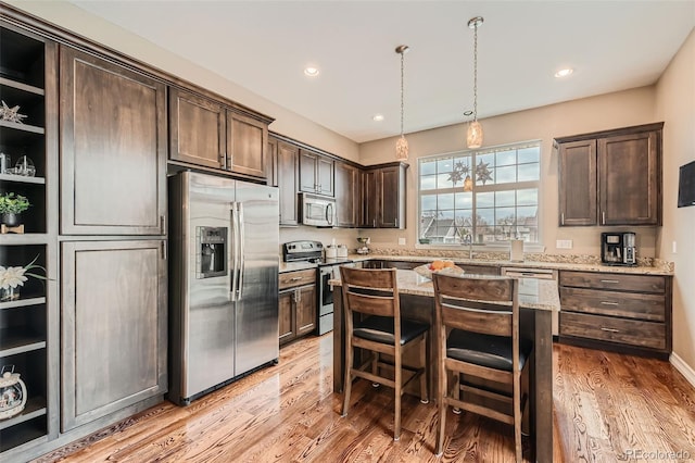 kitchen with light stone counters, dark brown cabinetry, a kitchen island, appliances with stainless steel finishes, and light wood finished floors