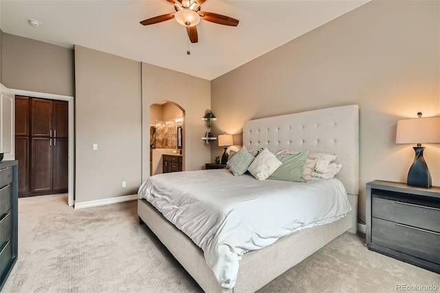 bedroom with baseboards, arched walkways, light colored carpet, ceiling fan, and ensuite bathroom