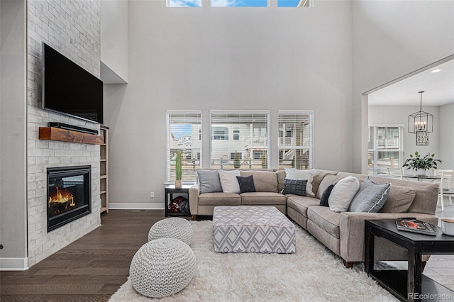 living room with a towering ceiling, a large fireplace, wood finished floors, baseboards, and a notable chandelier