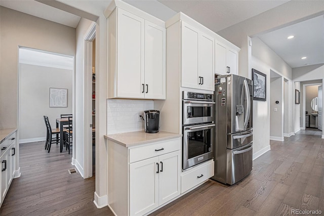 kitchen featuring dark wood-style flooring, stainless steel appliances, backsplash, and light countertops