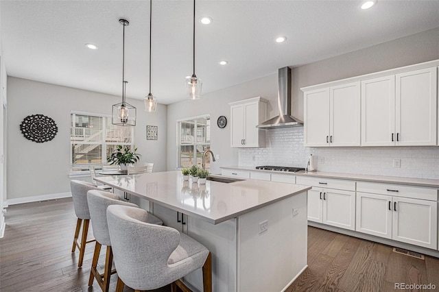 kitchen featuring a sink, wall chimney exhaust hood, gas stovetop, dark wood-type flooring, and backsplash