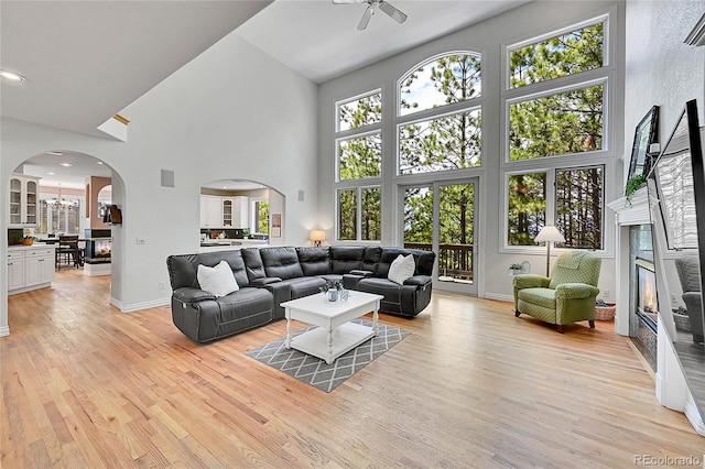 6681 Flintwood Rd, Parker, CO 80138 - living room featuring arched walkways, a high ceiling, a glass covered fireplace, a ceiling fan, and light wood-type flooring