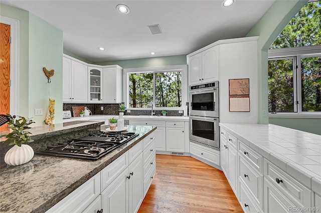 6681 Flintwood Rd, Parker, CO 80138 - kitchen featuring stainless steel double oven, black gas stovetop, recessed lighting, light wood-style flooring, and glass insert cabinets