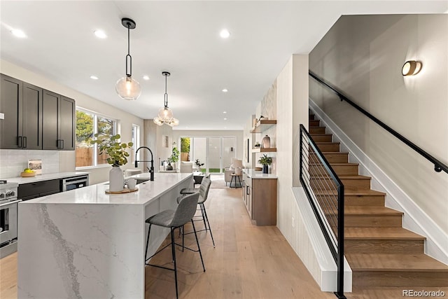 kitchen featuring light stone counters, light wood-style flooring, a kitchen island with sink, decorative backsplash, and a kitchen bar