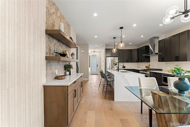 kitchen featuring open shelves, wall chimney range hood, a kitchen bar, appliances with stainless steel finishes, and a sink