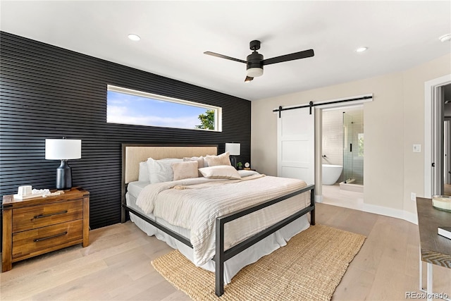 bedroom with a barn door, recessed lighting, light wood-style floors, and baseboards